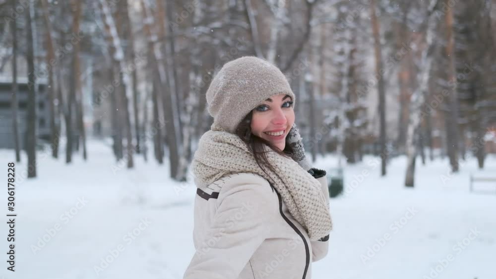 a beautiful young woman goes her back in a winter park, then turns and smiles while looking at the camera. slow motion a beautiful young woman goes her back in a winter park, then turns and smiles while looking at the camera. slow motion