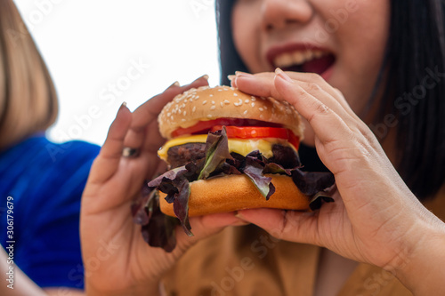 Hungry overweight woman smiling and holding hamburger and sitting in the living room, her very happy and enjoy to eat fast food. Concept of binge eating disorder (BED).