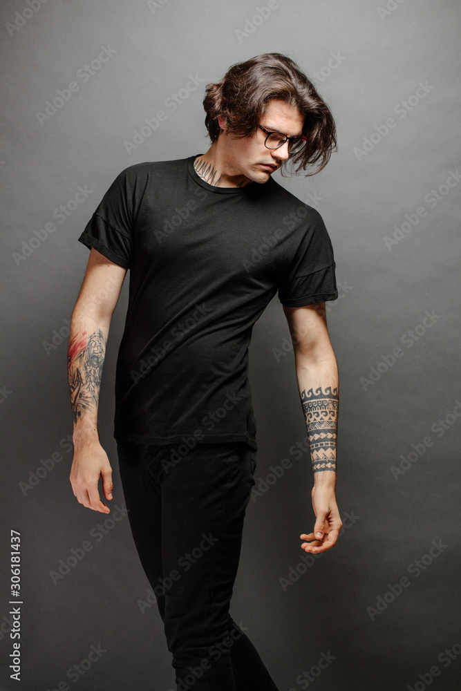 Hipster handsome male model with glasses wearing black blank t-shirt and black jeans with space for your logo or design in casual urban style