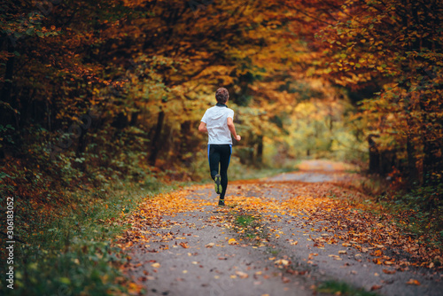 Runner trains in the picturesque autumn nature surrounded by colorful forest.