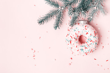 Christmas toy glazed donut with sugar sprinkling hanging on Christmas tree branch. Pink pastel background