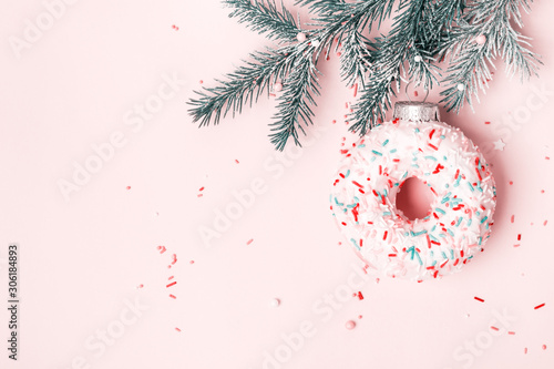 Christmas toy glazed donut with sugar sprinkling hanging on Christmas tree branch. Pink pastel background photo