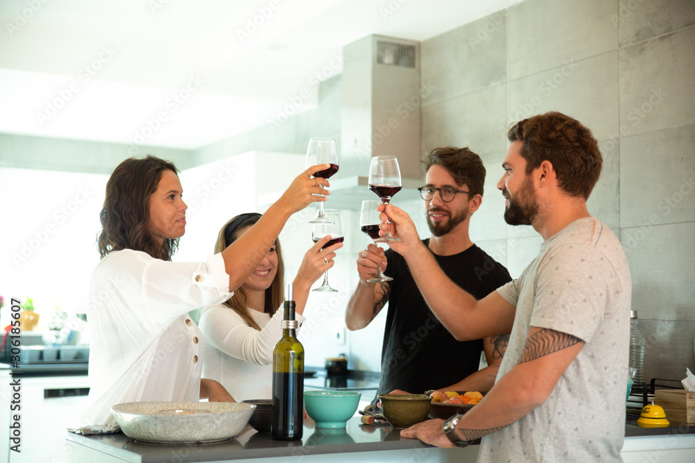 Happy positive friends celebrating event and toasting wine in kitchen. Young men and women in casual meeting indoors. Drinking wine at home concept Happy positive friends celebrating event and toasting wine in kitchen. Young men and women in casual meeting indoors. Drinking wine at home concept