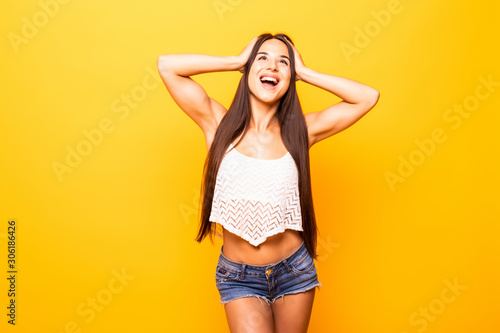 Portrait of cheerful young woman celebrating success wearing white shirt standing isolated over yellow background