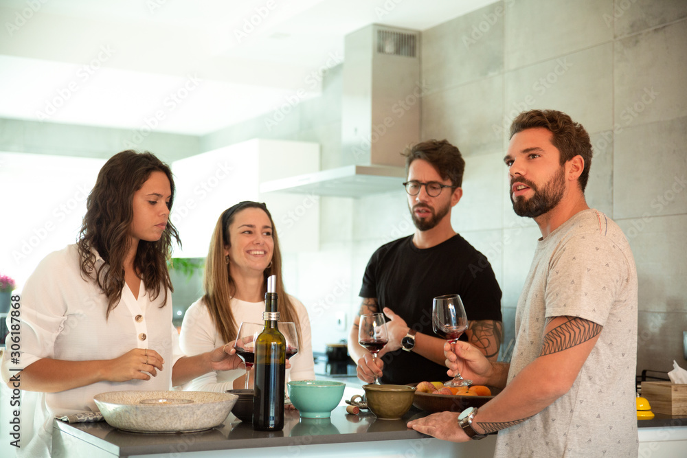 Team of friends chatting over glass of wine in kitchen. Young men and women in casual meeting indoors. Friendship concept Team of friends chatting over glass of wine in kitchen. Young men and women in casual meeting indoors. Friendship concept