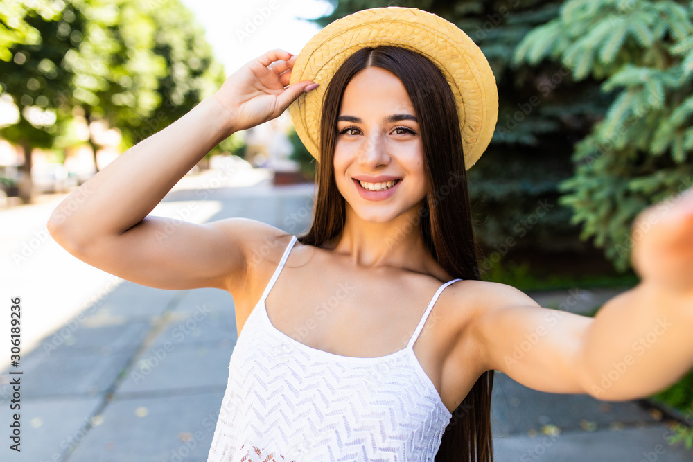 Young pretty woman in straw hat taking selfie on the summer street