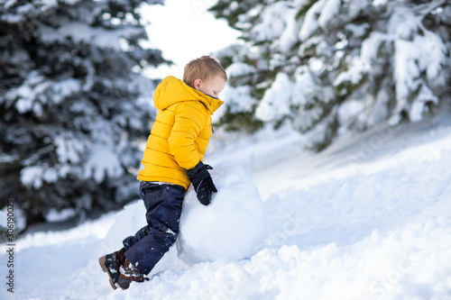 Little adorable boy building snowman. Playing with snow ball. winter cold time. Smiling and laughing