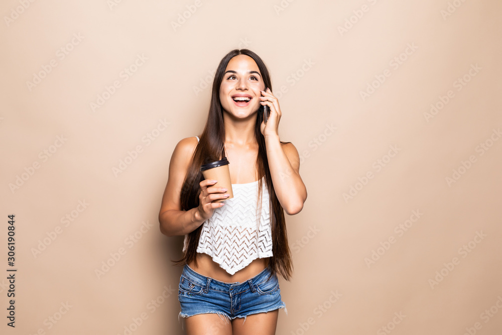 Young pretty woman with coffee cup talking on the phone on the beige background Young pretty woman with coffee cup talking on the phone on the beige background