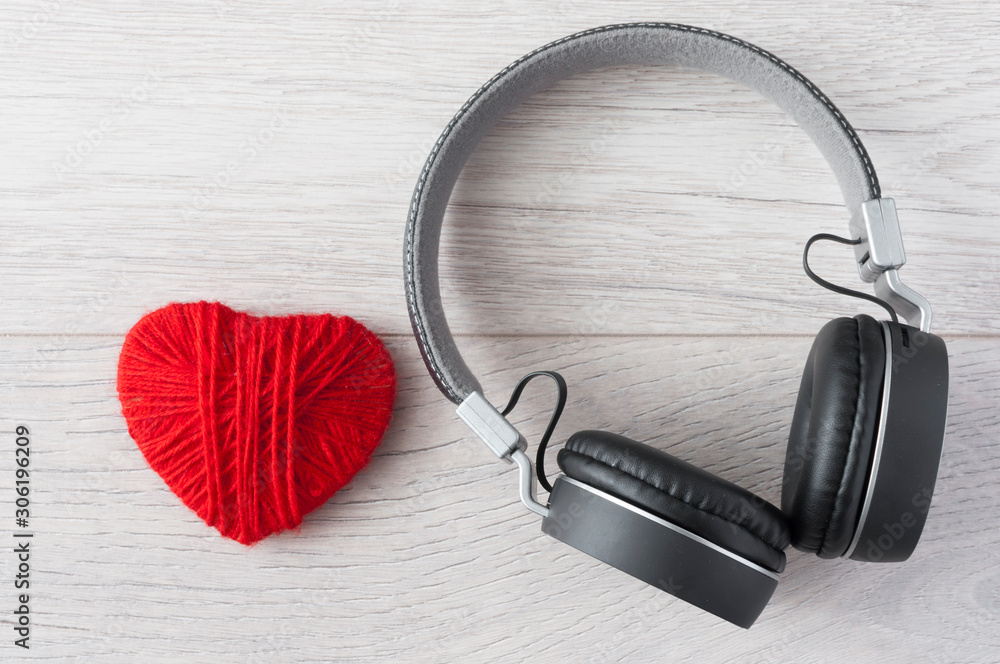 Top view of an black audio headphone with knitted red heart on white wooden background. Top view of an black audio headphone with knitted red heart on white wooden background.