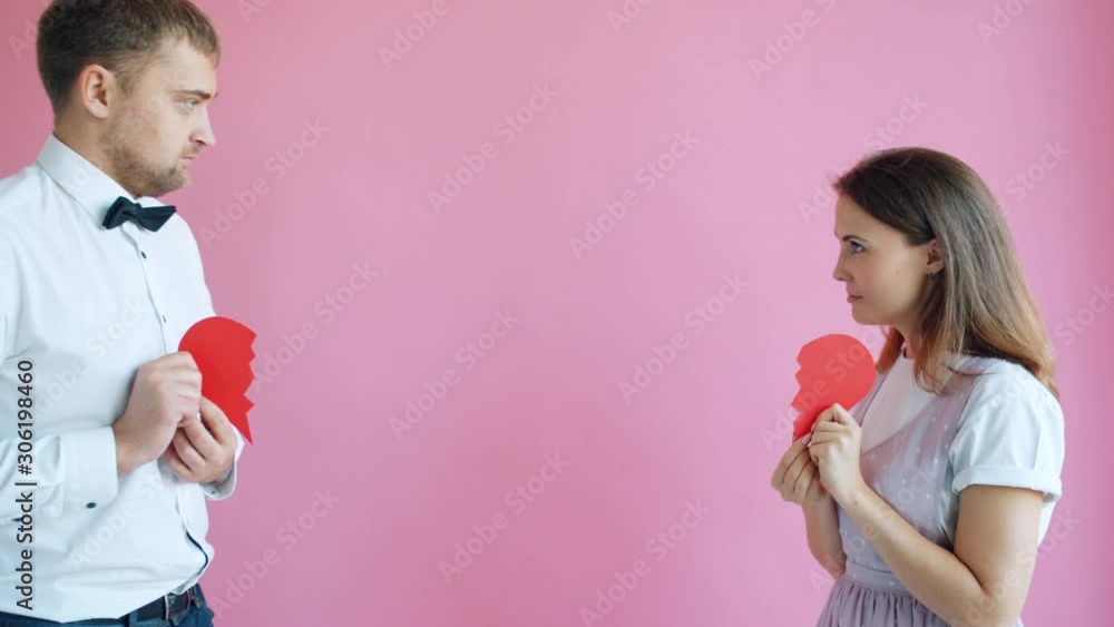 Man and woman are holding halves of heart stepping aside expressing separation and broken love. Troubled relations, youth and human emotions concept. Man and woman are holding halves of heart stepping aside expressing separation and broken love. Troubled relations, youth and human emotions concept.