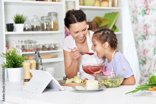 Portrait of cute little girl with her mother cooking together at kitchen table