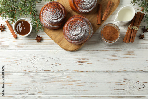 Cinnamon rolls  caramel  milk and fir branches on white wooden background  top view