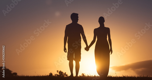 Fotografie Man and woman walking together holding hands at sunset