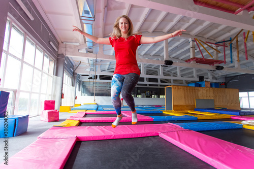 Fitness, fun, leisure and sport activity concept - Young happy woman jumping on a trampoline indoors