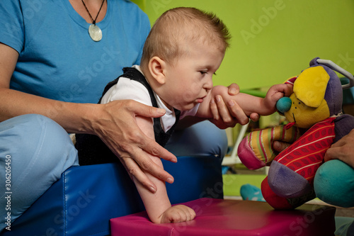 Portrait of a baby with cerebral palsy on physiotherapy in a children therapy center. Boy with disability has therapy by doing exercises. Little kid has musculoskeletal therapy in rehabitation centre.