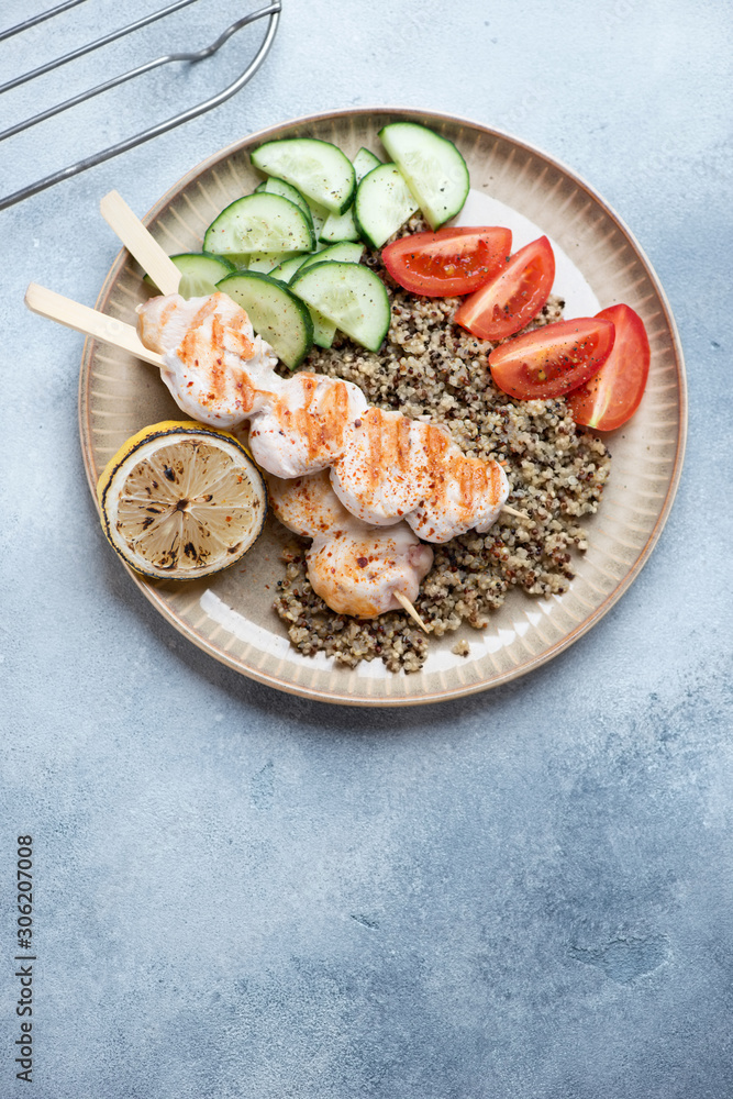 Chicken skewers with quinoa and fresh vegetables, flatlay over light-blue stone background with copyspace, vertical shot Chicken skewers with quinoa and fresh vegetables, flatlay over light-blue stone background with copyspace, vertical shot