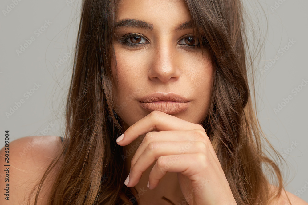 Headshot of beautiful Caucasian brunette posing in front of grey background. Beauty photography. Headshot of beautiful Caucasian brunette posing in front of grey background. Beauty photography.