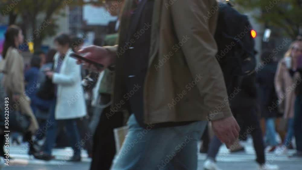 TOKYO, JAPAN - NOV 2019 : Crowd of people at Shibuya Scramble Crossing in busy early evening rush hour. Many commuters and tourists at the street. Shot in sunset time. In front focus. Slow motion. TOKYO, JAPAN - NOV 2019 : Crowd of people at Shibuya Scramble Crossing in busy early evening rush hour. Many commuters and tourists at the street. Shot in sunset time. In front focus. Slow motion.
