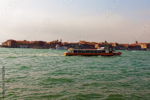 The vaporetto is a Venetian public waterbus. Travel and tourism concept. Landscape with Venetian Lagoon and buildings at the background. Autumn sunny day. Venice, Italy