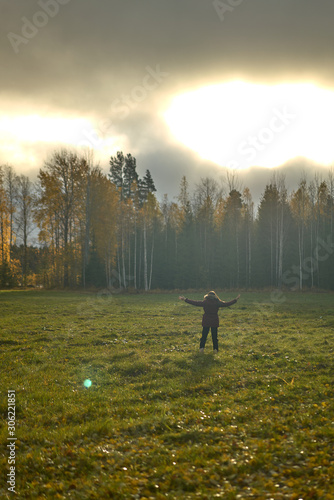 Person with open arms in the middle of a field surrounded by forest.incredible misty sky