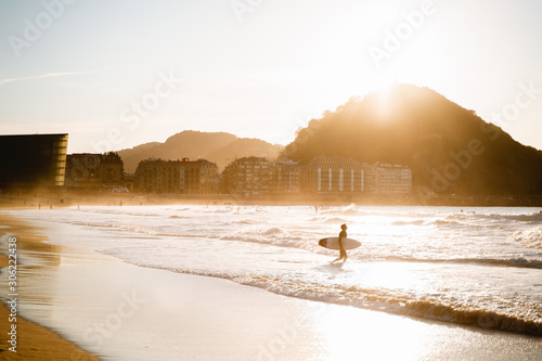 Surfer enters to the water on Zurriola Beach in San Sebastian during sunset