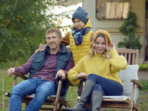 Happy stylish European family sitting on bench near camper van, they like to travel and enjoy their holidays.
