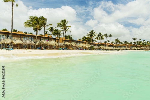 Beautiful view of white sand Aruba beach. Blue sunbeds under sun umbrellas on turquoise water and blue sky with white clouds background. Eagle Beach of Aruba Island.
