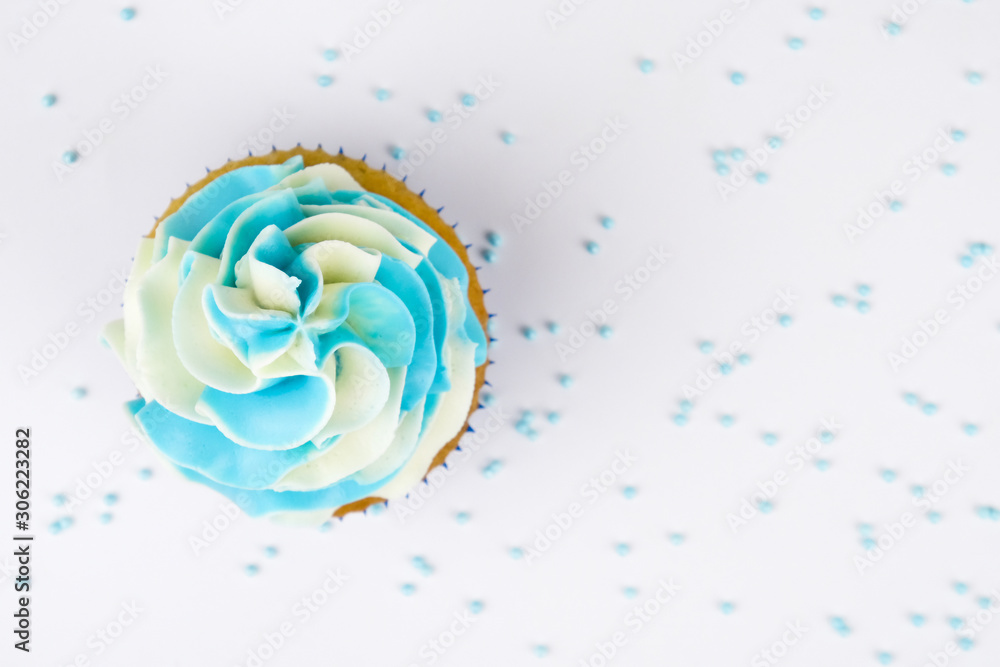 Cupcake on birthday with blue and white cream on white background, decorated with sprinkles. Top view.