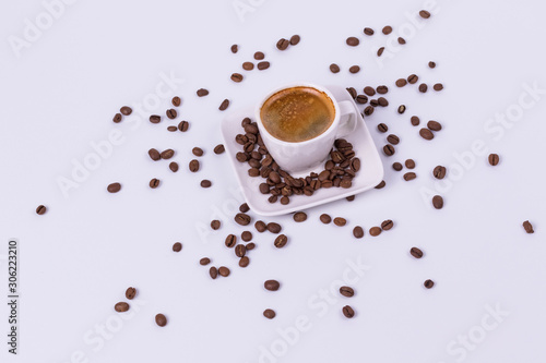 Hot coffee in a cup, coffee beans are scattered nearby. White background, top view