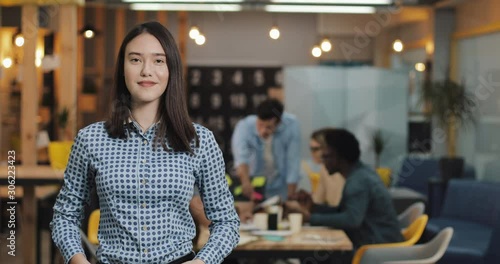 Young businesswoman standing in the modern office, smiling and looking into the camera. Working people on the blurred background. photo