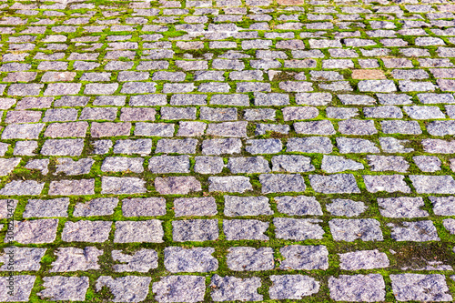 The street is covered with gray paving stones. Seams overgrown with green moss. texture of old roads.