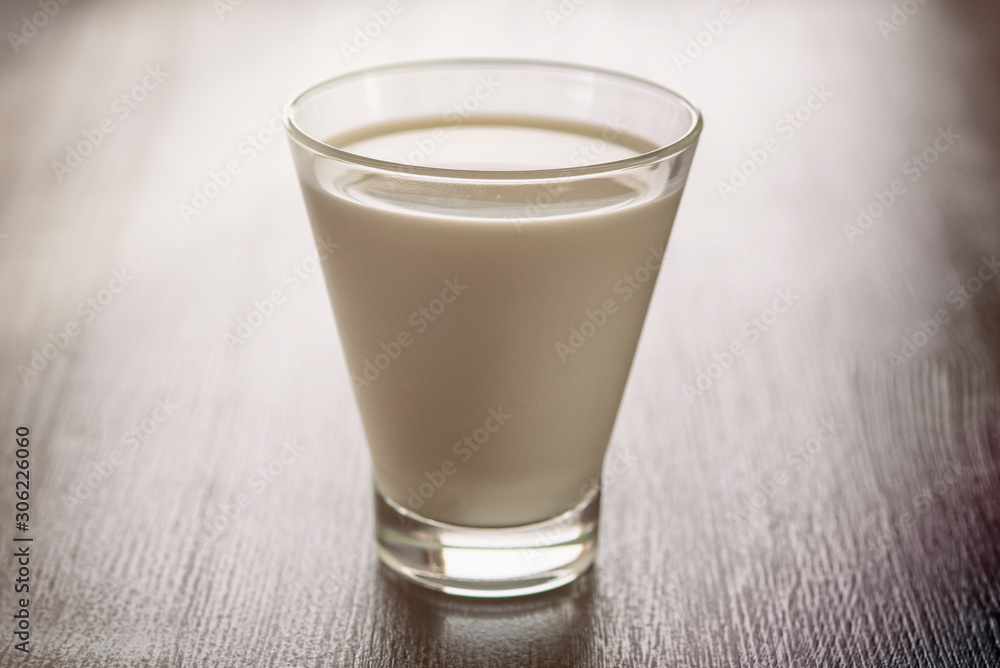 Milk in a glass cup on a wooden background. Photographed close-up in a low key. Milk in a glass cup on a wooden background. Photographed close-up in a low key.