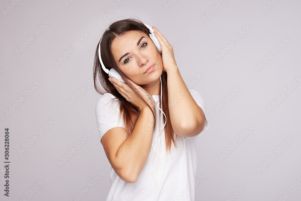 Attractive woman in casual wear, smiles gently and foxy, uses modern cell phone, listens music via headphones, chooses favorite track, poses against grey background. People, active lifestyle content. Attractive woman in casual wear, smiles gently and foxy, uses modern cell phone, listens music via headphones, chooses favorite track, poses against grey background. People, active lifestyle content.