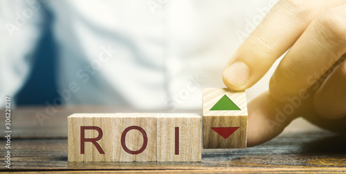 Wooden blocks with the word ROI and green arrow up. High level of business profitability. Return on investment, invested capital, rate. Success. Growth. Analytics. Report photo