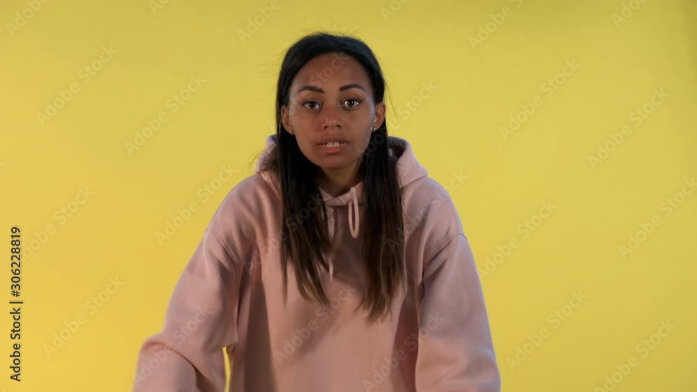 Mixed-race young woman swearing at somebody on yellow background. She is angry and nervous. Mixed-race young woman swearing at somebody on yellow background. She is angry and nervous.