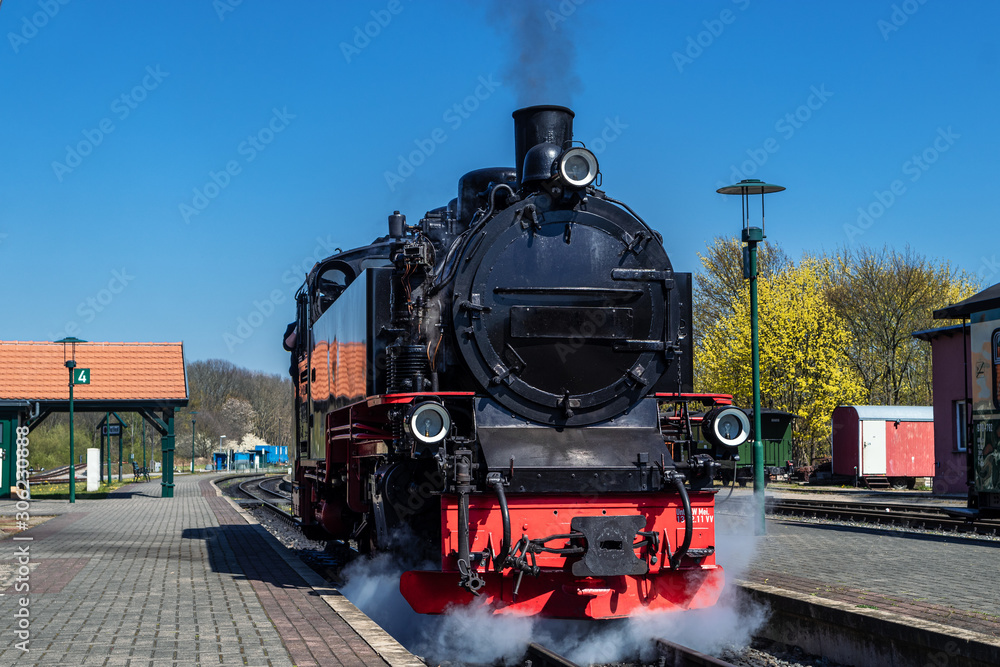 Fototapeta premium Lokomotywa parowa na peronie, na początku pod parą na tle błękitnego nieba