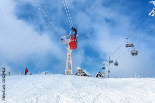 Seilbahn, Schwebebahn vor blaumem Himmel mit vereistem Mast, neben Sessellift, mit Berghütte im Hintergrund