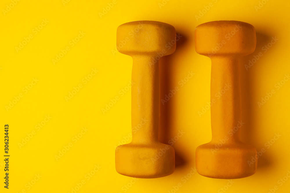 yellow dumbbells lie on a yellow background, the concept of summer, training, sports yellow dumbbells lie on a yellow background, the concept of summer, training, sports