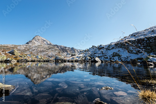 Reflection of mountain peak in clear fresh water of alpin pond after first snow close to Lago Bianco at Bernina pass Switzerland