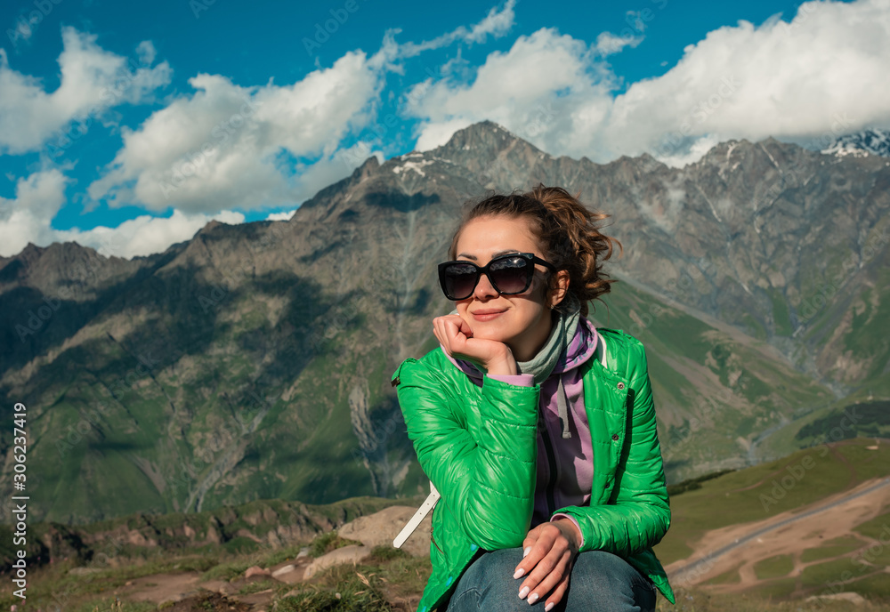 Curly woman sitting on top peak of mountains in summer during holidays. Beautiful young female girl looking to camera. Young woman outdoors. Lifestyle concept.
