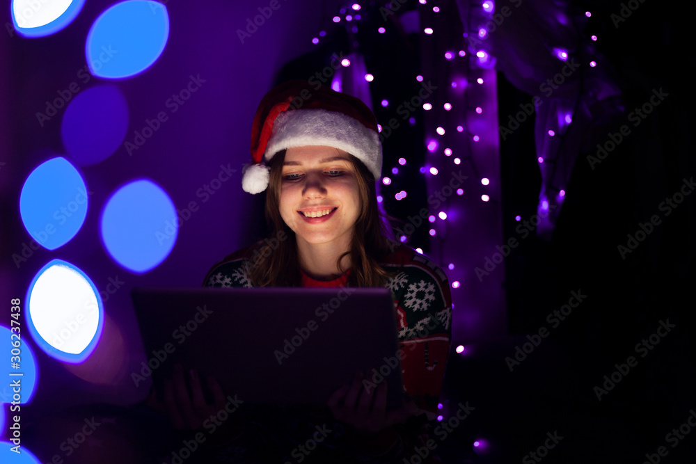 young girl with a laptop in the New Year sits at home in Christmas clothes, a woman online for Christmas young girl with a laptop in the New Year sits at home in Christmas clothes, a woman online for Christmas