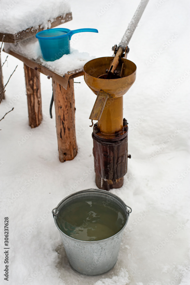 Bucket of clean drinking water stands next to the well and the hand pump in a village courtyard. Bucket of clean drinking water stands next to the well and the hand pump in a village courtyard.