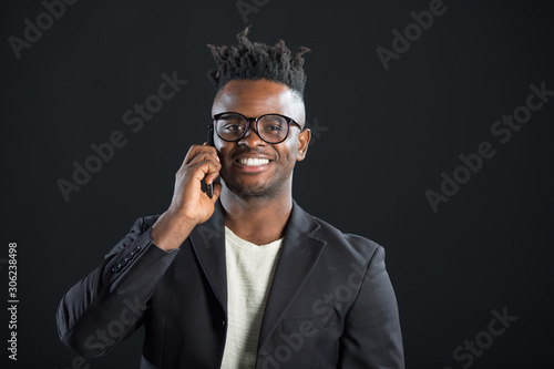handsome african man in a suit on a black background with glasses with a phone in his hand