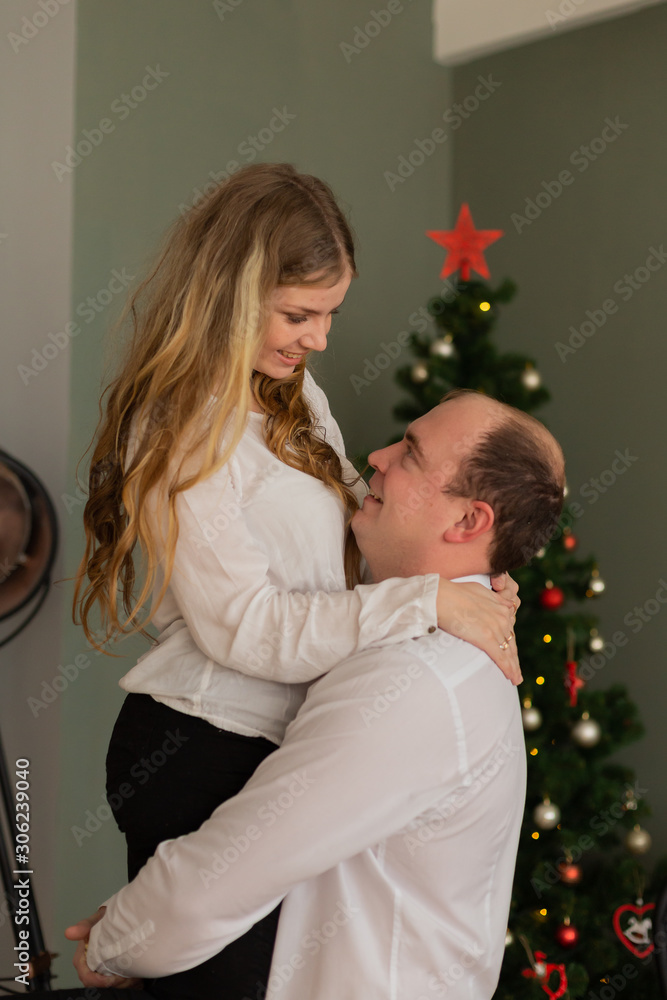 Happy husband and wife at the Christmas tree at home. Husband holds his wife in his arms. Happy husband and wife at the Christmas tree at home. Husband holds his wife in his arms.