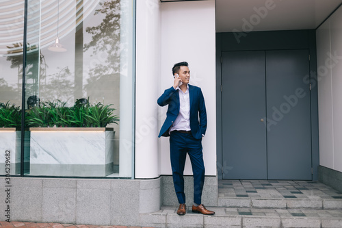 Young Asian businessman talking on smartphone near glass fence and doors