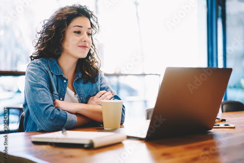 Successful female student watching positive movie via famous website in internet world using 4g wireless connection on modern laptop computer, caucasian woman interested on online webinar via netbook photo