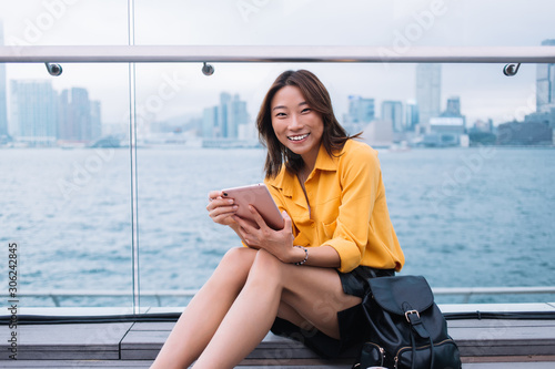 Smiling ethnic woman sitting with tablet on urban pier