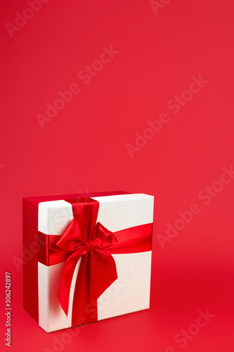 Pretty minimalist christmas gift box with ribbon isolated over red background. © Screaghin