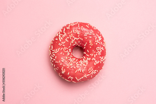 Sweet pink donut with white sprinkles on a pink background flat lay