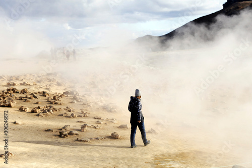 Woman walking in volcanic landscape in Iceland. Boiling mudpots in the geothermal area Hverir and cracked ground around. Location: geothermal area Hverir, Myvatn region, North part of Iceland, Europe 